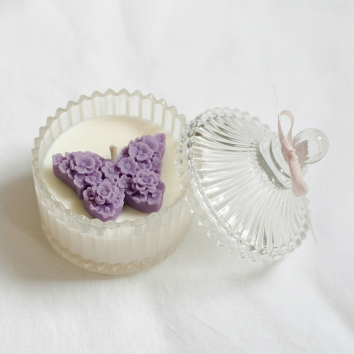 Candle with purple floral decorations in a glass holder on a white background