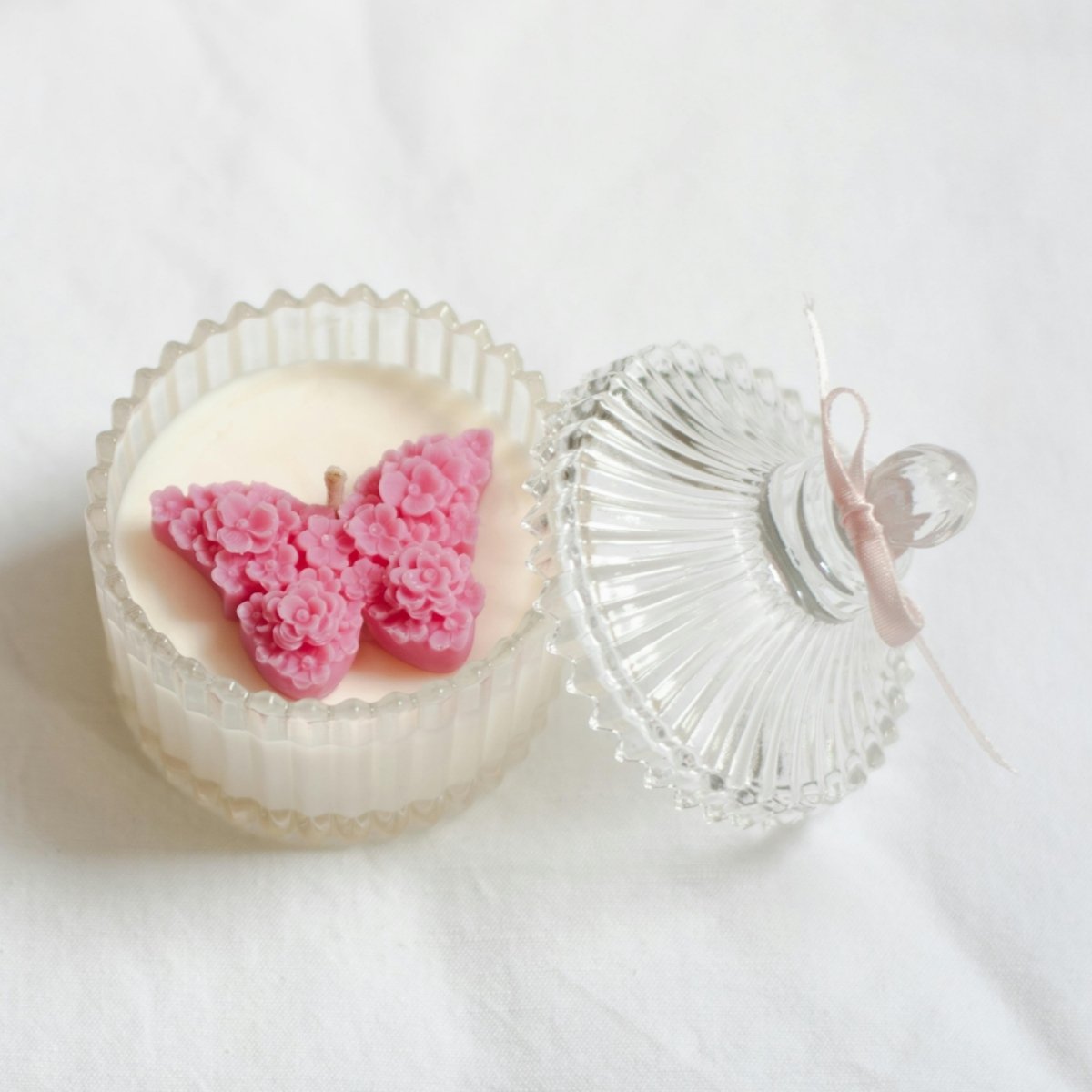 Candle with pink butterfly-shaped flowers in a glass container on a white background