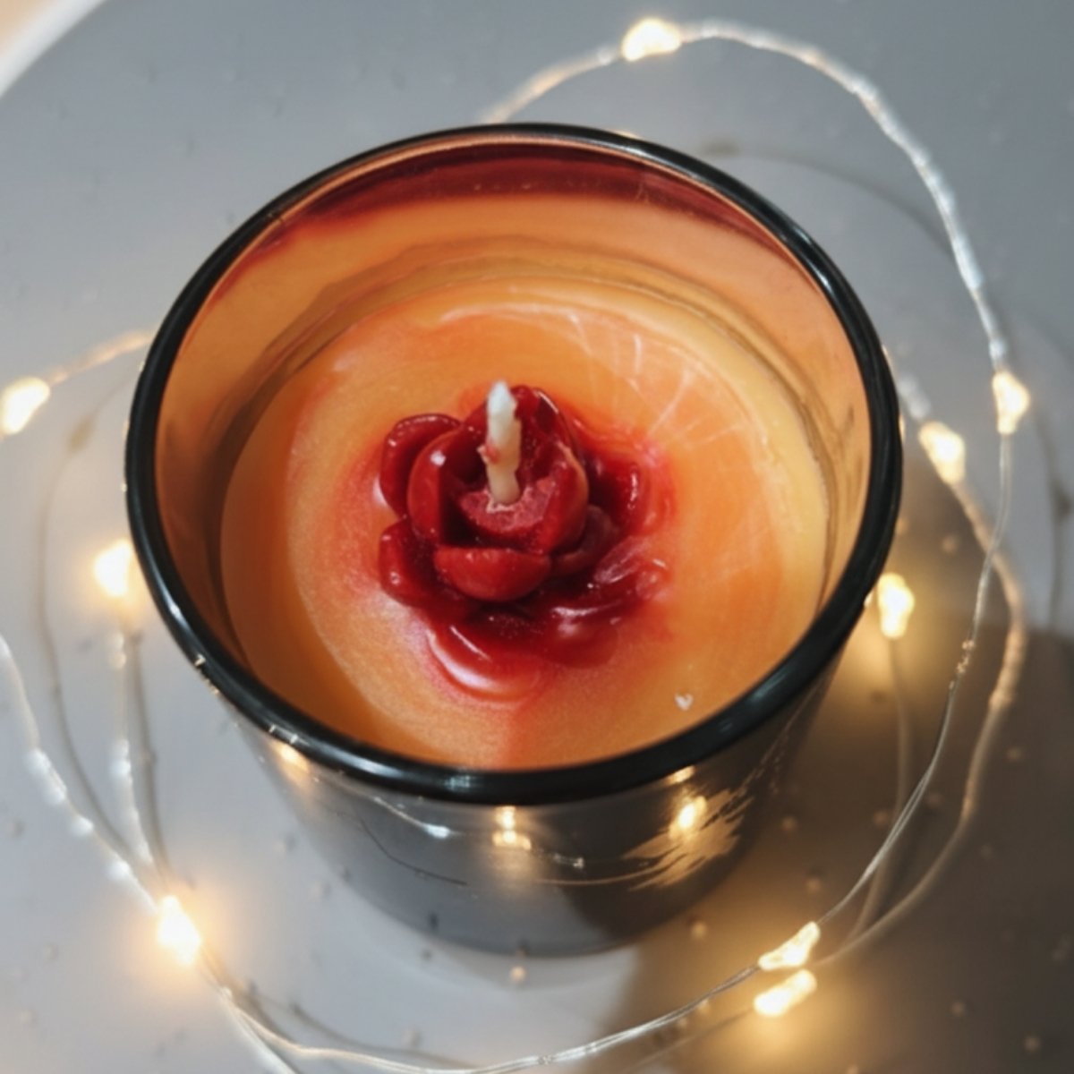 Magical fairy candle in black jar with orange wax and red flower inside, exterior visible