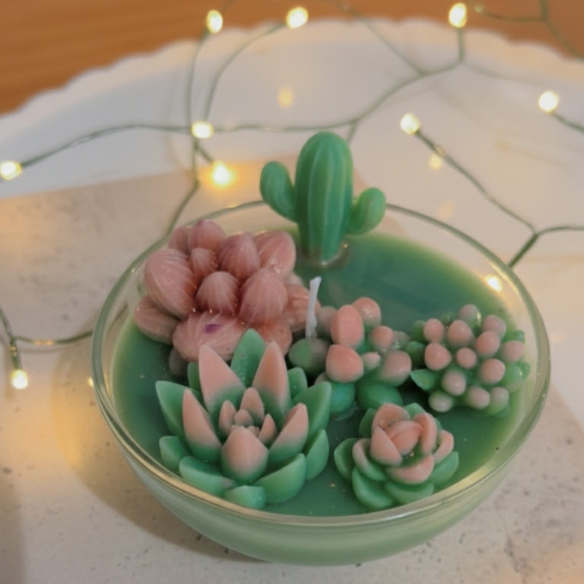 Candle with succulent plant designs in a glass bowl on a textured surface with string lights
