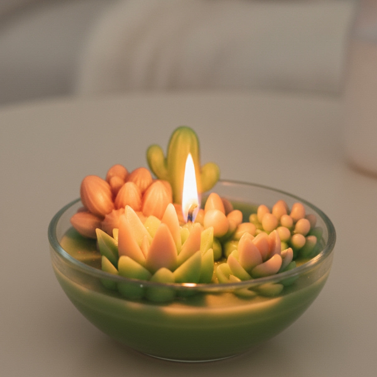 Candle shaped like a succulent plant with a lit wick in a glass bowl.
