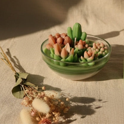 Candle shaped like a succulent plant in a glass bowl on a textured surface.