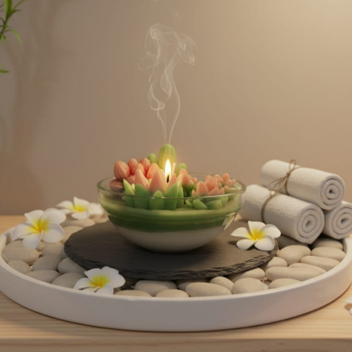 Candle with fruit in a bowl on pebbles with flowers and rolled towels in the background