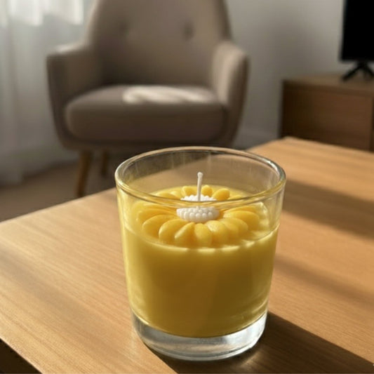 Yellow candle in a glass holder on a wooden table with a blurred chair and curtain in the background